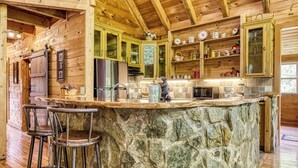 A rustic kitchen with wooden cabinets, a stone island, and bar stools. - Glori's Retreat - $560 of FREE  tickets for each paid day (Pigeon Forge)