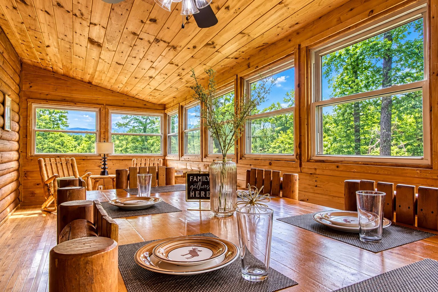 Een houten hutje interieur met een eettafel voor vier personen, grote ramen en uitzicht op groen.