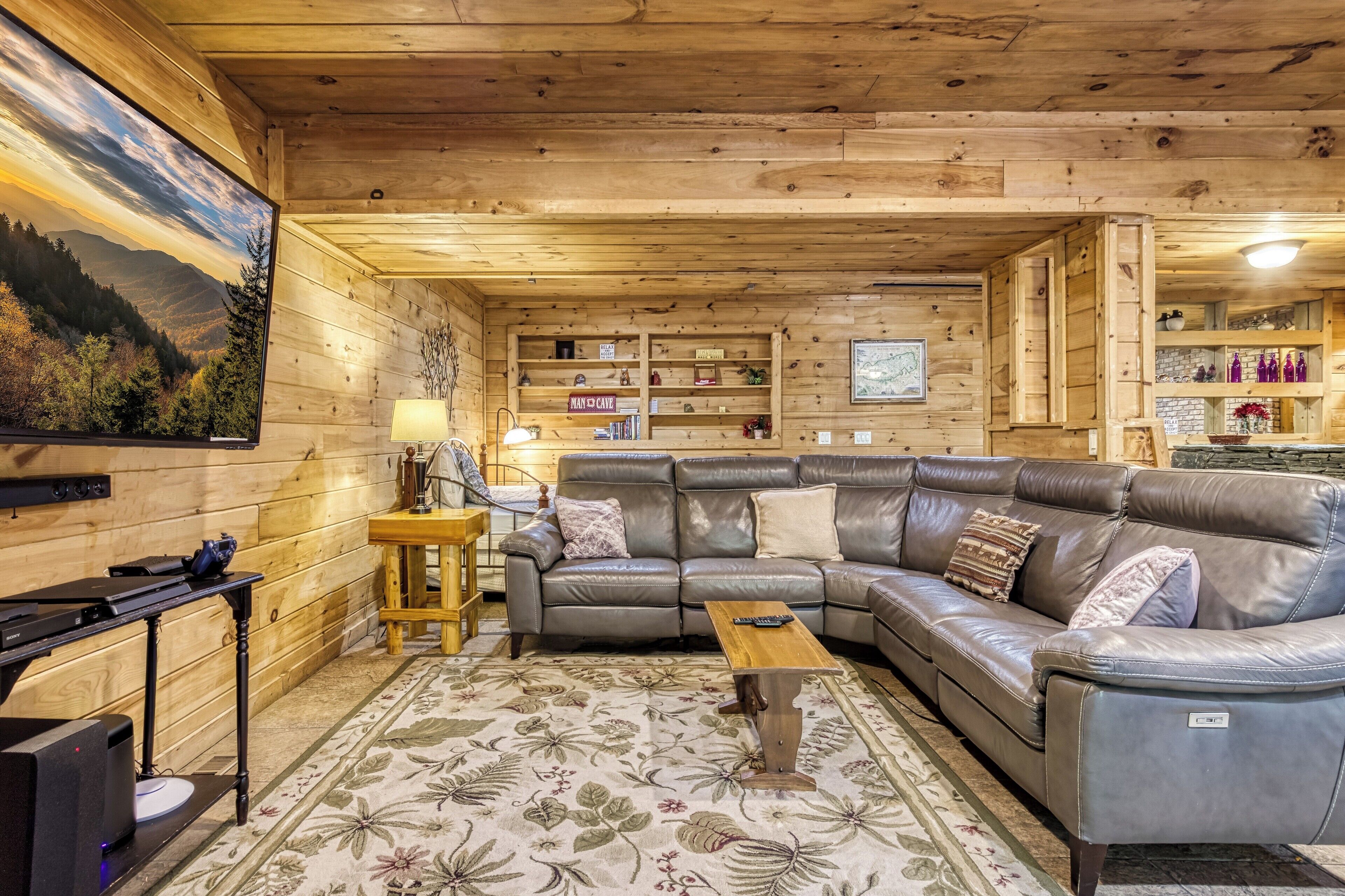 A cozy cabin interior with a leather sofa, wooden shelves, and a fireplace.