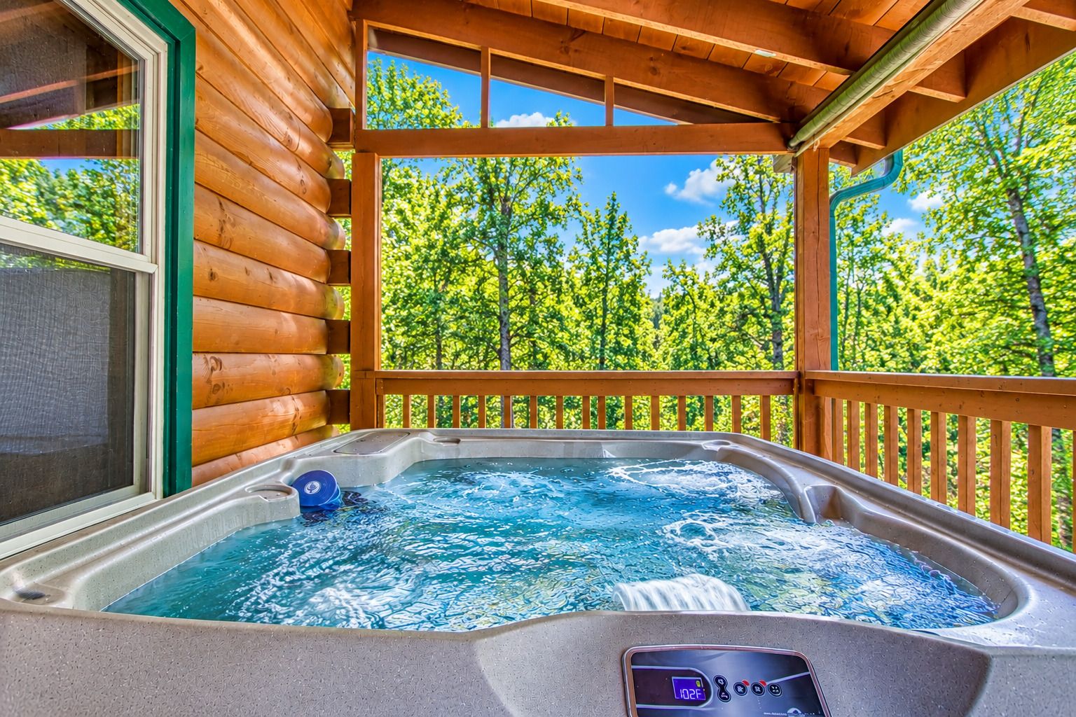 A hot tub with a digital display, surrounded by wooden deck and a view of a forest.