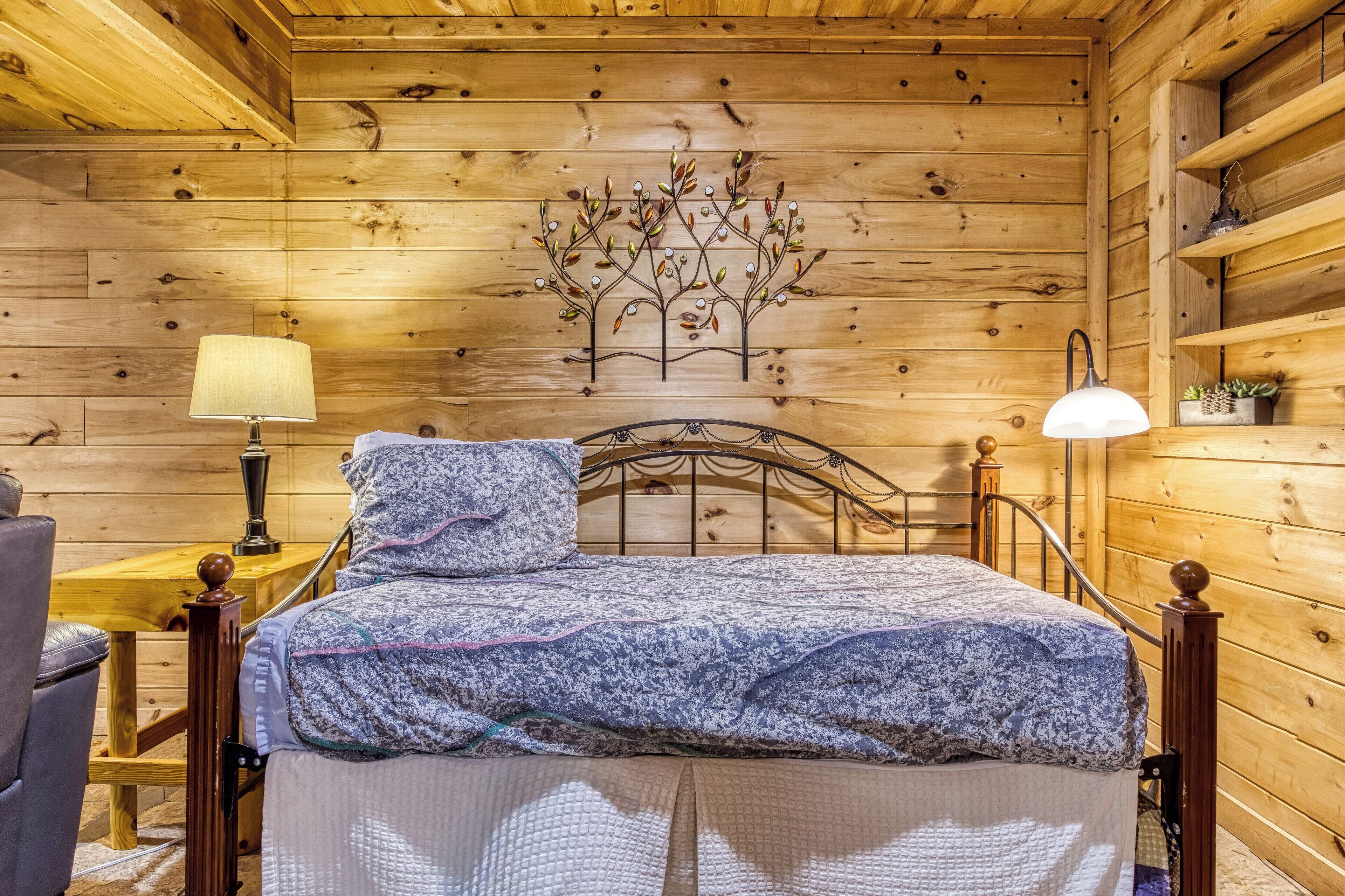 Une chambre dans une cabane en bois, avec un lit, deux lampes de chevet, une décoration murale représentant un arbre et une étagère en bois ornée de plantes.