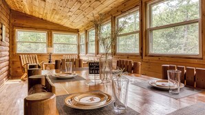 A wooden cabin interior with a dining table set for four, large windows, and a sign reading "FAMILY PATRONS HERE". - Glori's Retreat - $560 of FREE  tickets for each paid day (Pigeon Forge)