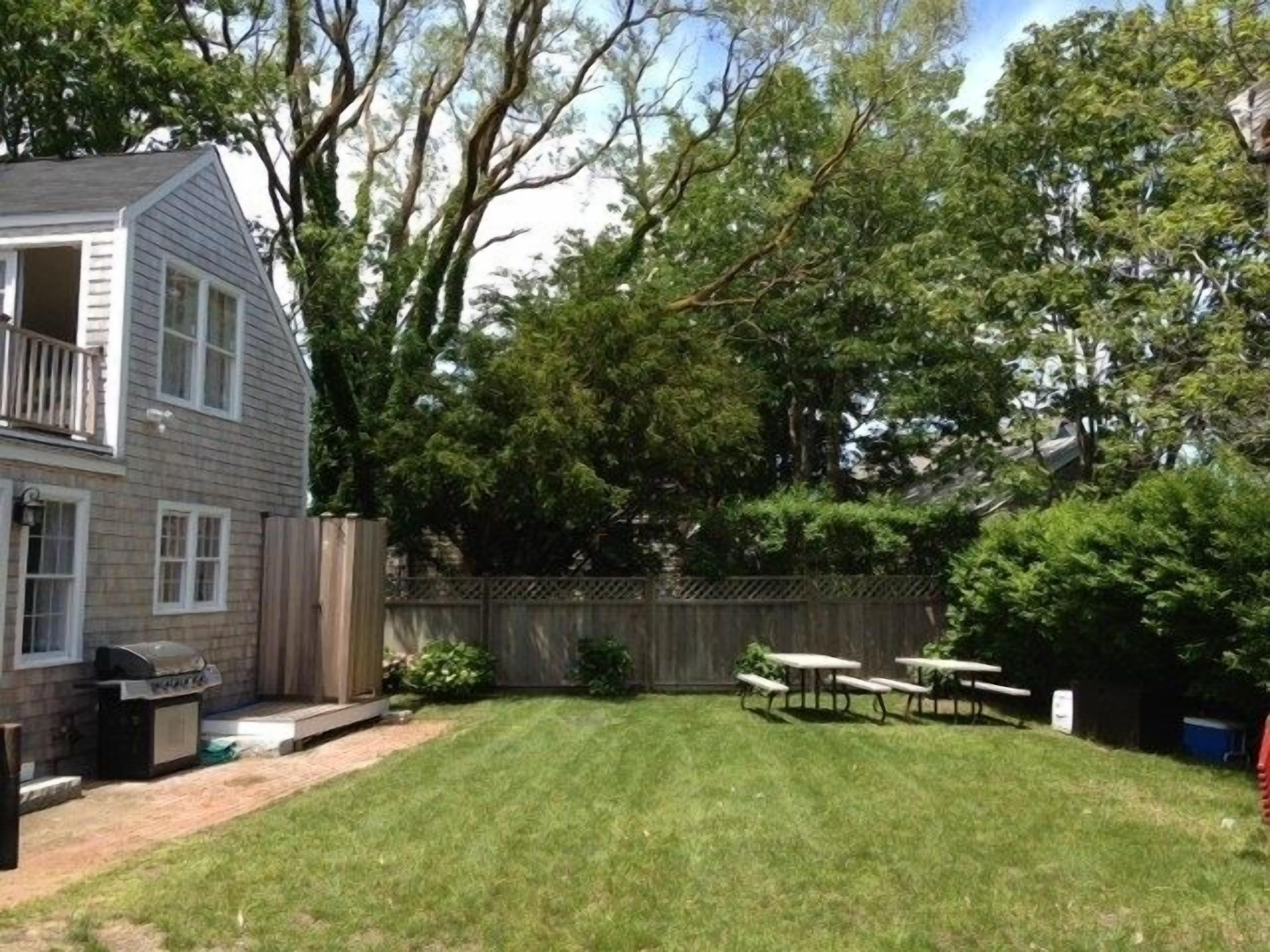 A backyard with a lawn, a barbecue grill, and picnic tables.
