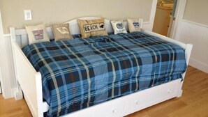 Cama branca com edredom xadrez azul e quatro travesseiros, um deles com a palavra 'BEACH'.