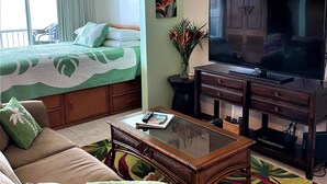 Un salon comprenant un canapé, une table basse, un téléviseur, un lit et un balcon.