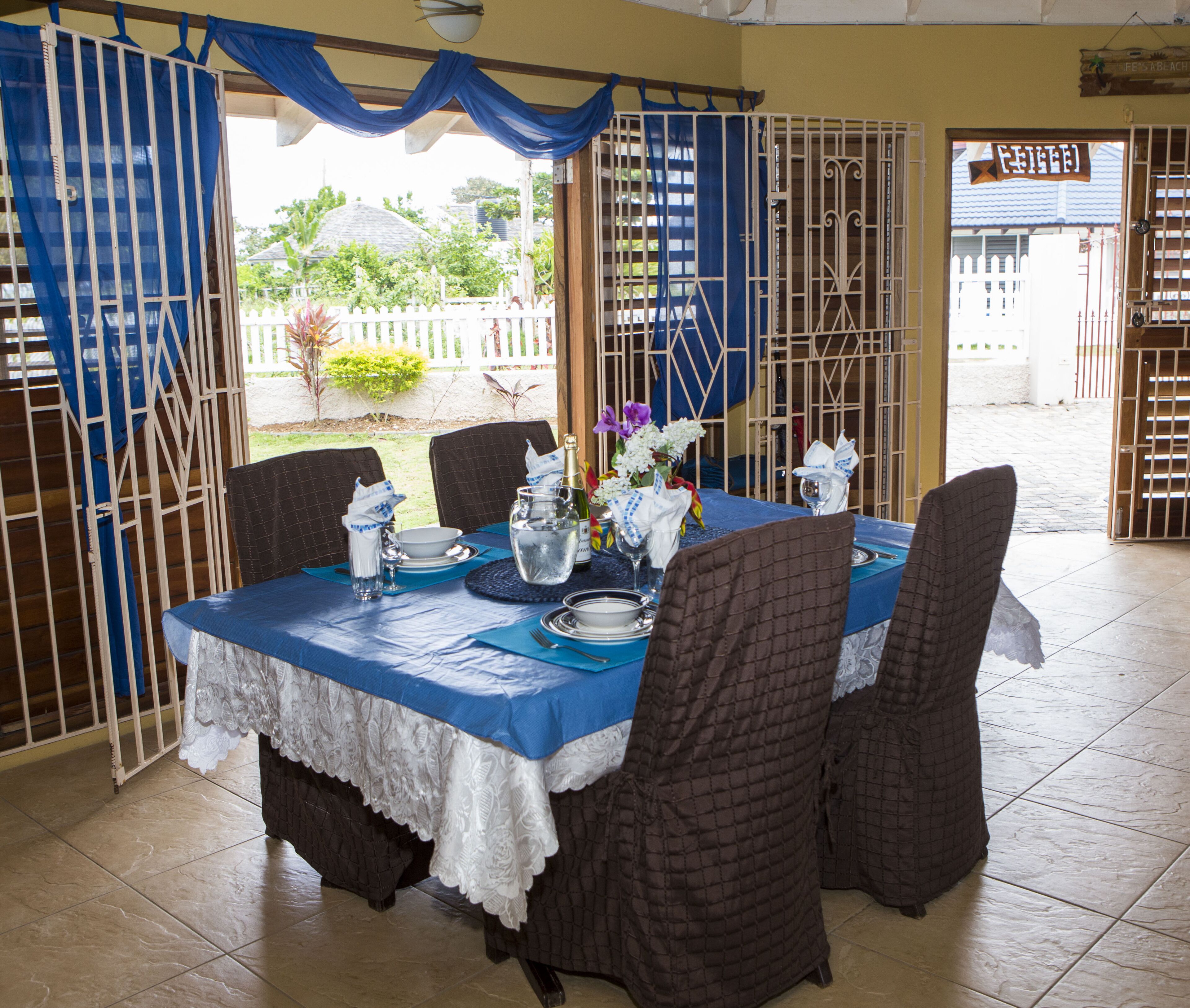 A dining area with a table set for two, featuring a blue tablecloth, white lace table runner, and brown upholstered chairs.