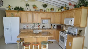 A kitchen with wooden cabinets, a white refrigerator, a microwave, and a stove. There are three stools with colorful seats. - DUPLEX IN DUCK KEY, 2 Bedroom /2 Bath  w/40' Dock,  Trailer Storage Incl. (Marathon)