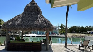 A thatched umbrella structure with a seating area, a pool, and a view of a house and palm trees. - DUPLEX IN DUCK KEY, 2 Bedroom /2 Bath  w/40' Dock,  Trailer Storage Incl. (Marathon)