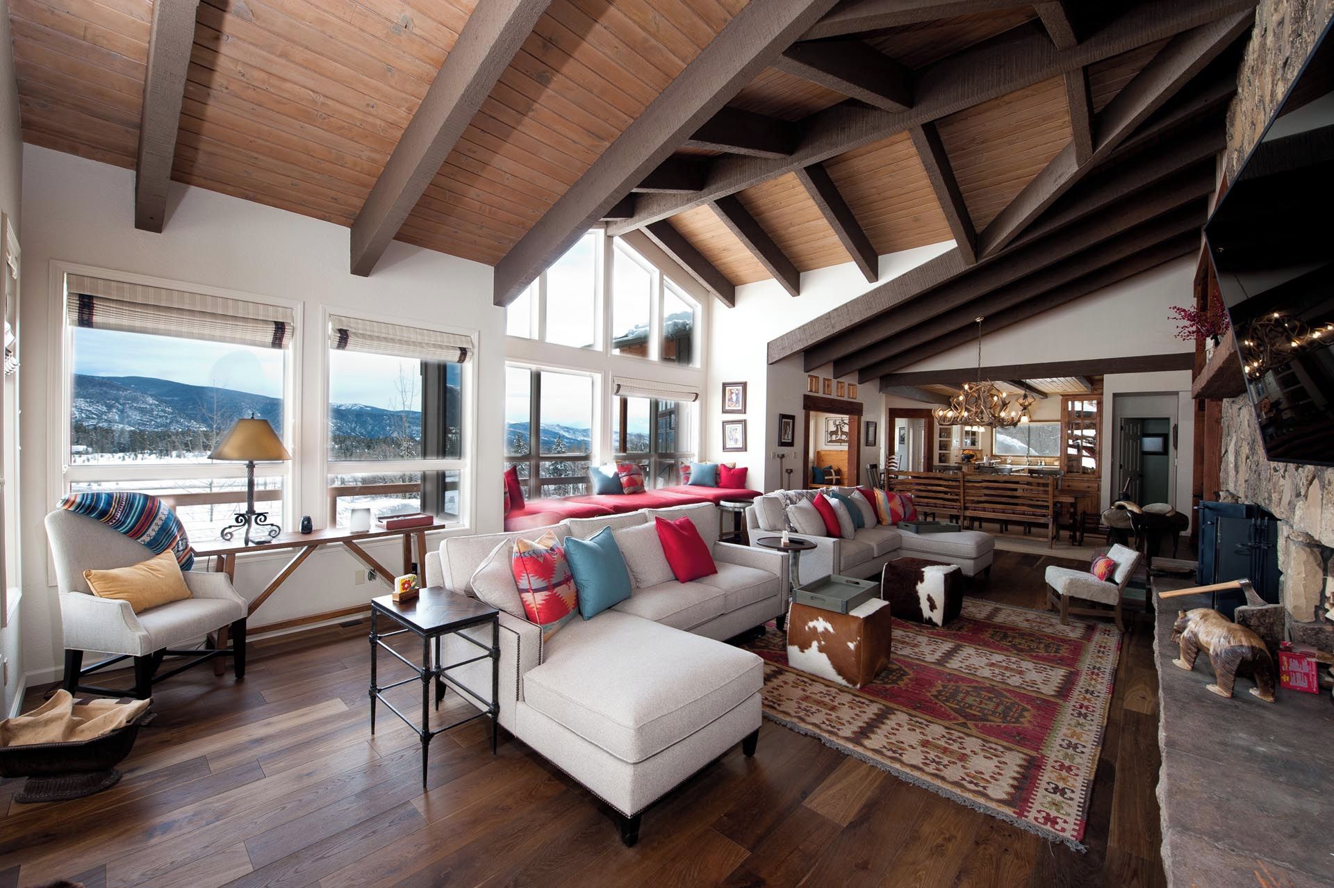 A spacious living area with a high wooden ceiling, large windows offering a view of a snowy landscape, and a cozy seating arrangement.