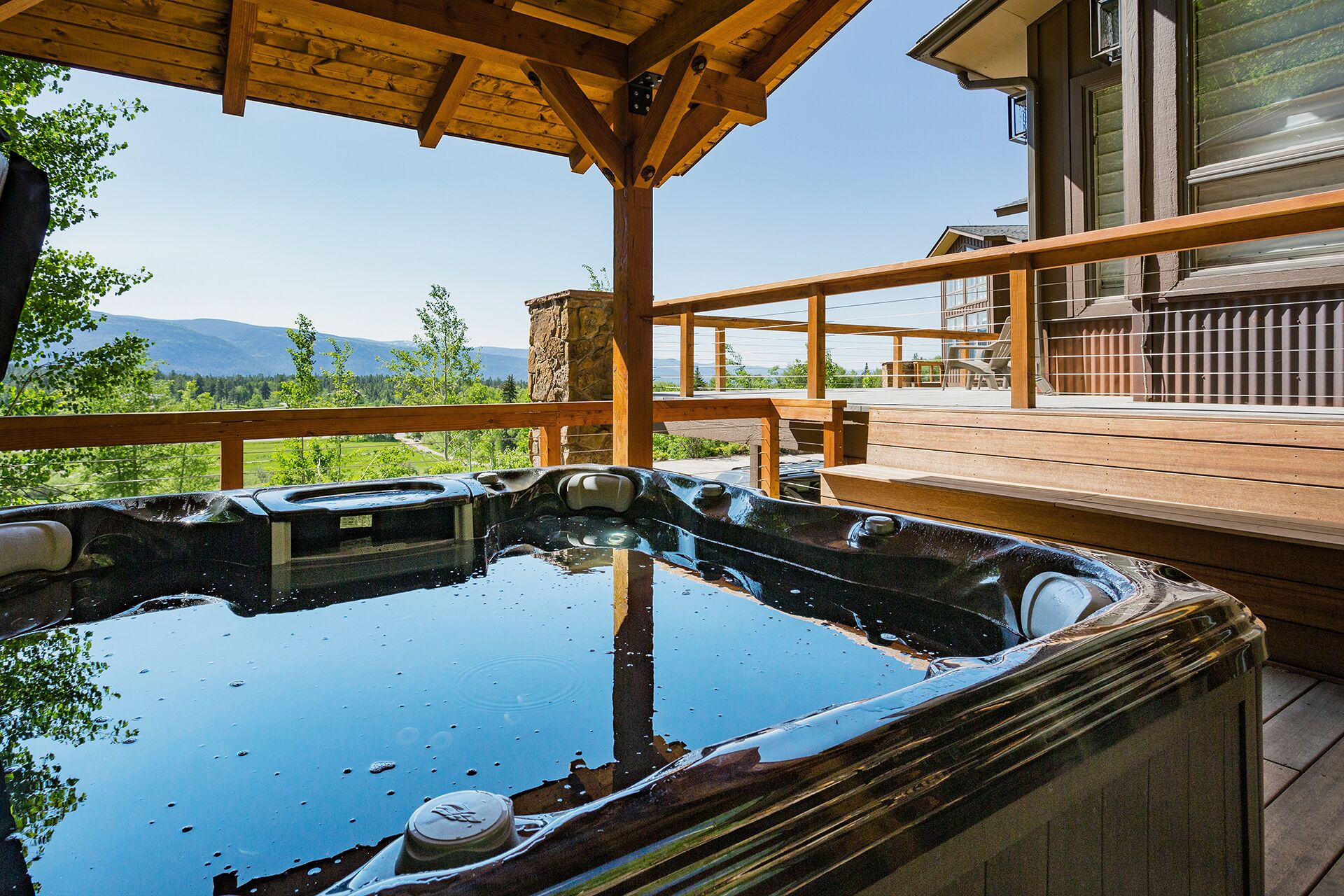 A hot tub on a wooden deck with a view of mountains and a house in the background.