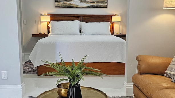 Camera da letto con un letto, lampade da comodino, un quadro, una pianta su un tavolino e un divano in pelle marrone.