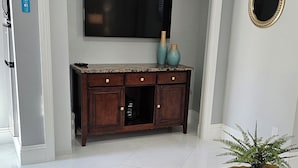 Un soggiorno con una TV a schermo piatto montata sopra un mobile in legno, un tavolino rotondo con una pianta e un tappeto grigio sul pavimento.