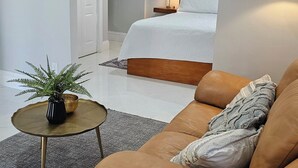 Una moderna camera d'albergo con un divano in pelle marrone, un piccolo tavolino con una pianta, un letto con una testiera in legno e un quadro appeso al muro.
