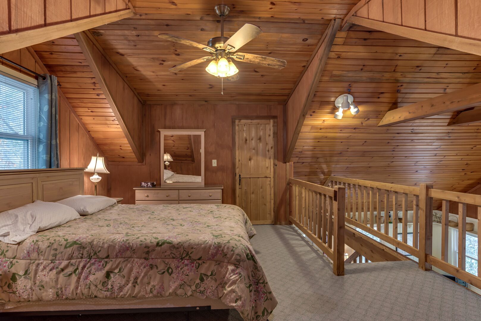 Une chambre à coucher comprenant un lit, une commode, un miroir, un ventilateur de plafond et un balcon avec une balustrade.