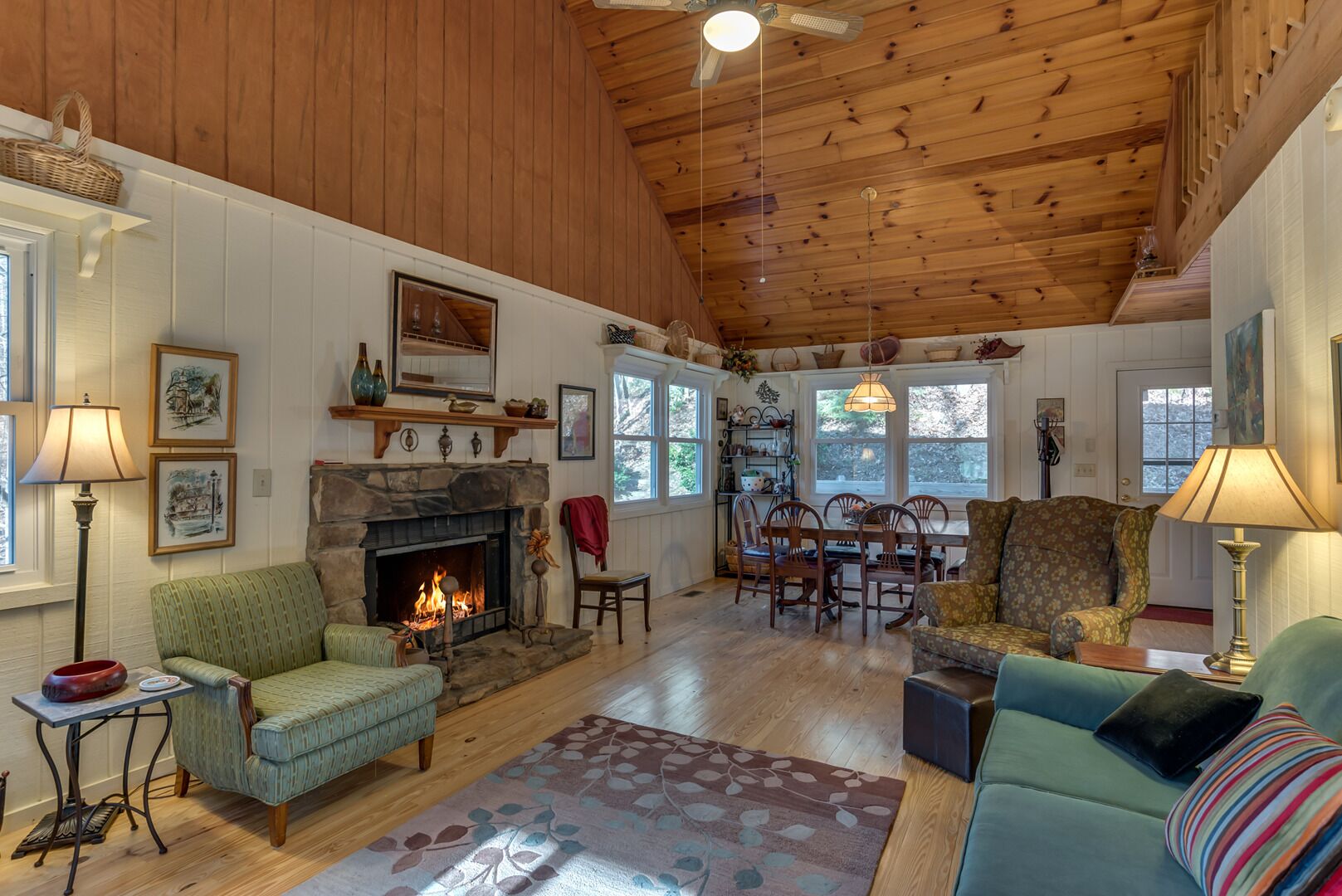 A cozy living room with a fireplace, wooden ceiling, and a dining area with chairs and a table.