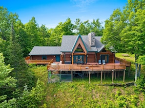 A log cabin with a deck, surrounded by dense forest. - Full Log Lodge 3 night minimum, 2 night  minimum  October- April, Pet Friendly  (Lakewood)