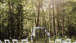 An outdoor wedding ceremony setup with white chairs arranged in rows, a decorated archway, and a forested background. - Full Log Lodge 3 night minimum, 2 night  minimum  October- April, Pet Friendly  (Lakewood)