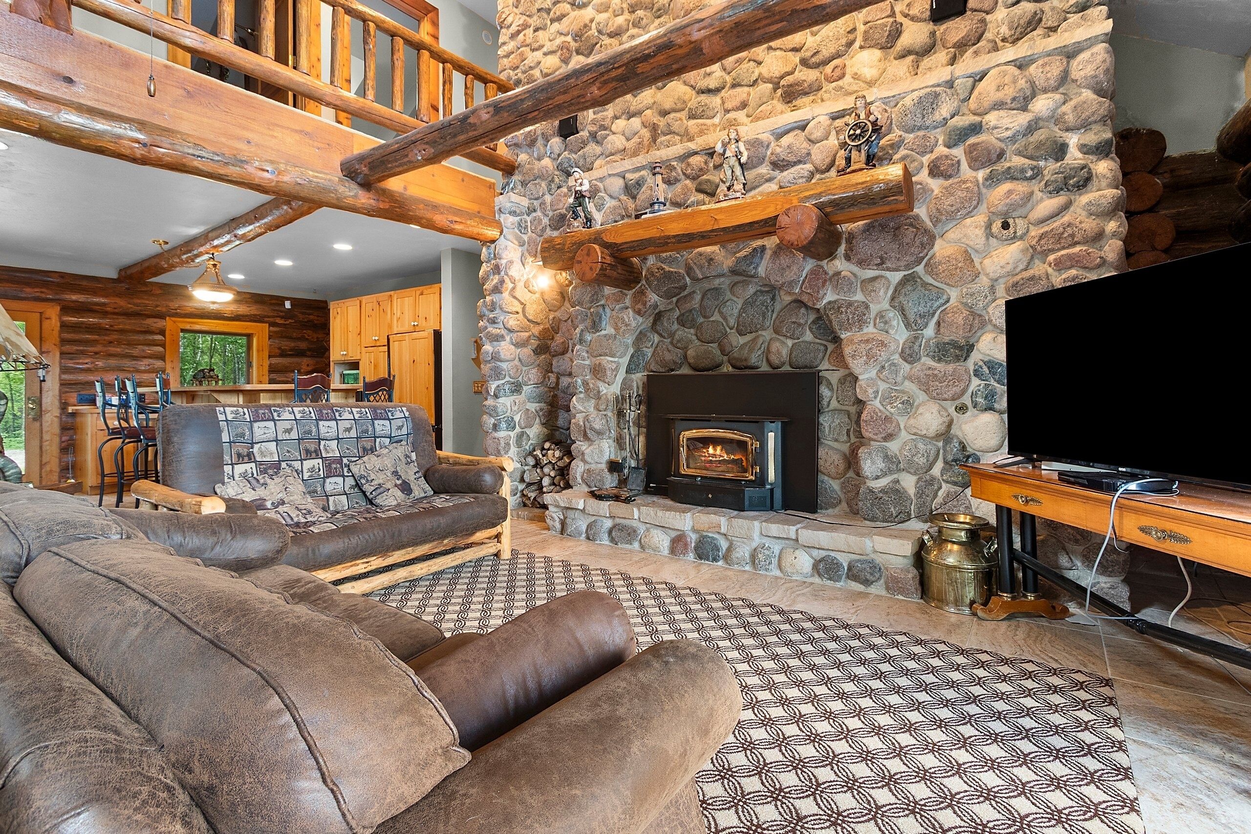 A cozy living room with a stone fireplace, wooden beams, a leather sofa, and a television.
