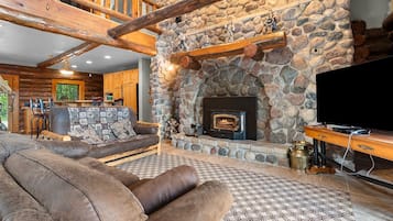 A cozy living room with a stone fireplace, wooden beams, a leather sofa, and a television.