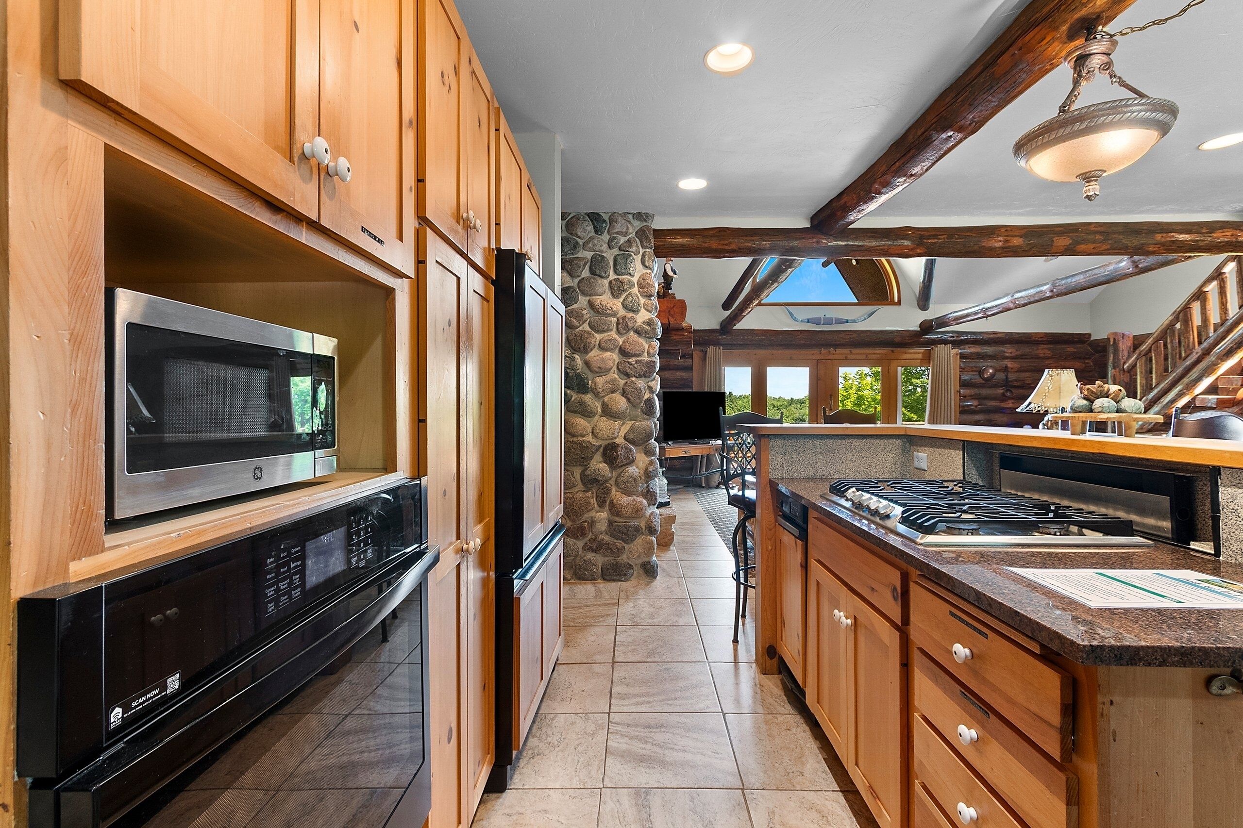 A kitchen with wooden cabinets, a microwave, a stove, and a stone wall.