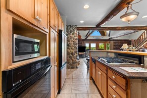 A kitchen with wooden cabinets, a microwave, a stove, and a stone wall. - Full Log Lodge 3 night minimum, 2 night  minimum  October- April, Pet Friendly  (Lakewood)
