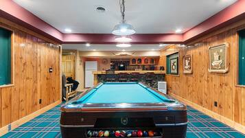 A pool table with a variety of balls, a bar area with stools, and wooden paneling on the walls.