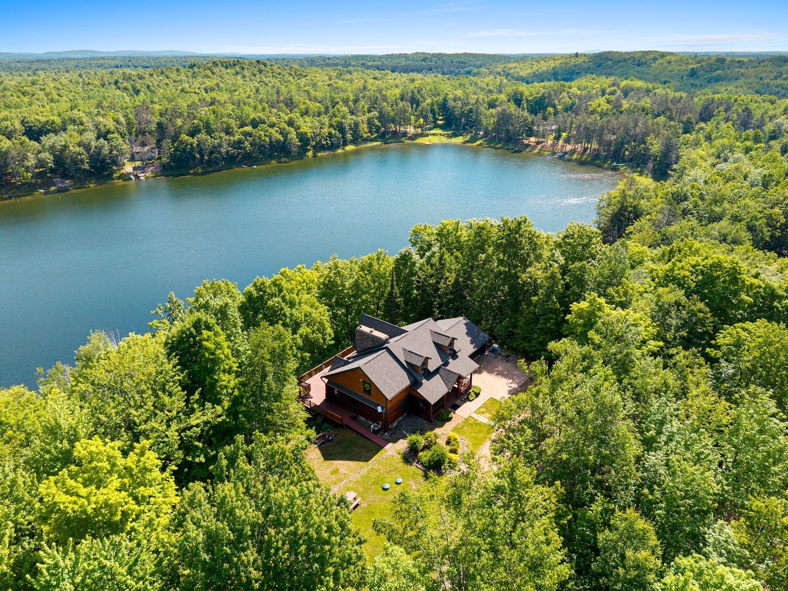 A cabin with a deck, surrounded by dense forest and a lake.