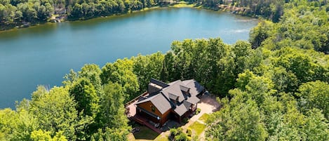 A cabin with a deck, surrounded by dense forest and a lake.