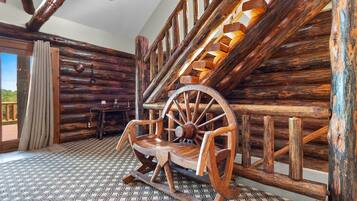 A rustic interior with a wooden rocking chair, a spinning wheel, and a patterned floor.