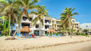 A beachfront hotel with multiple balconies, palm trees, and beach chairs. - Ground Floor Beachfront 2 BR 2 BA condo with Wifi and AC (Akumal)