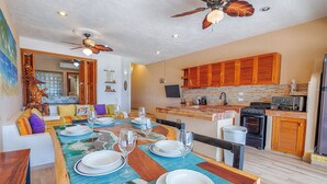 A dining area with a wooden table set for four, a kitchen with wooden cabinets and a stove, and a ceiling fan. - Ground Floor Beachfront 2 BR 2 BA condo with Wifi and AC (Akumal)