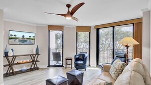 Un salon moderne avec un ventilateur de plafond, un canapé, un fauteuil, une table basse et un téléviseur fixé au mur.