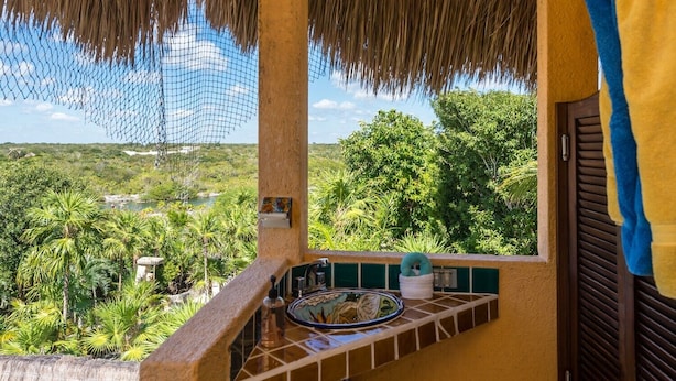 A balcony with a view of a lush landscape, a tiled backsplash, and a hanging net. - One-of-a-Kind Akumal Villa – Eclectic Design, Pool & Private Lagoon Access (Akumal)