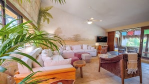 A spacious living room with a large sofa, a coffee table, and a TV. There are plants and a ceiling fan. - One-of-a-Kind Akumal Villa – Eclectic Design, Pool & Private Lagoon Access (Akumal)