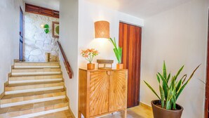 A staircase with a stone wall, a wooden cabinet with a woven basket, and a potted plant. - One-of-a-Kind Akumal Villa – Eclectic Design, Pool & Private Lagoon Access (Akumal)