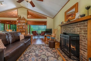 Cozy living room with a fireplace, comfortable seating, and a large window offering a view of the outdoors.