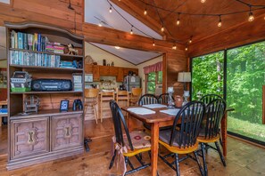 Cozy cabin-style room with a dining table, bookshelf, and large window offering a forest view.