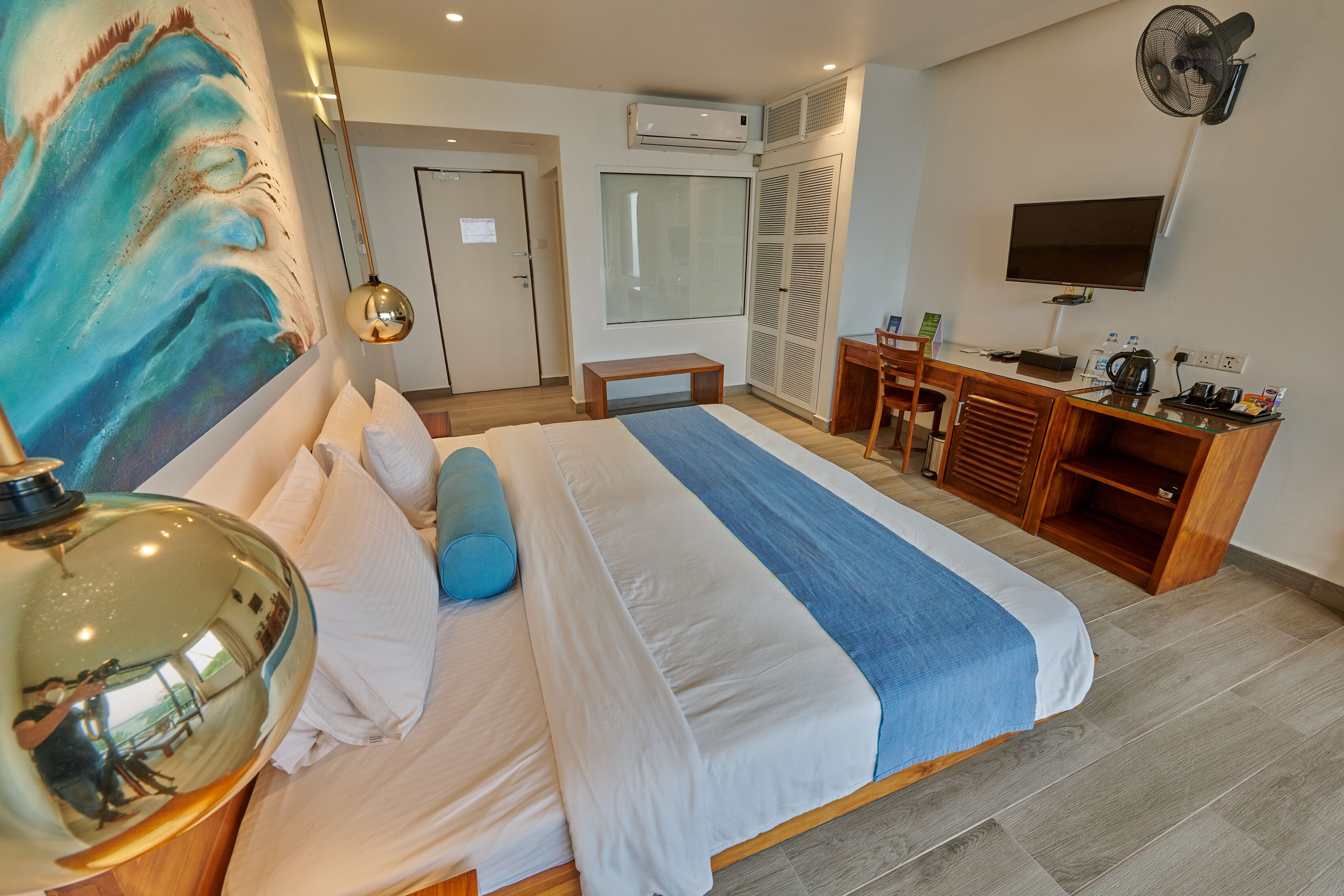 A modern hotel room with a large bed, a desk, a chair, a TV, and a wardrobe.