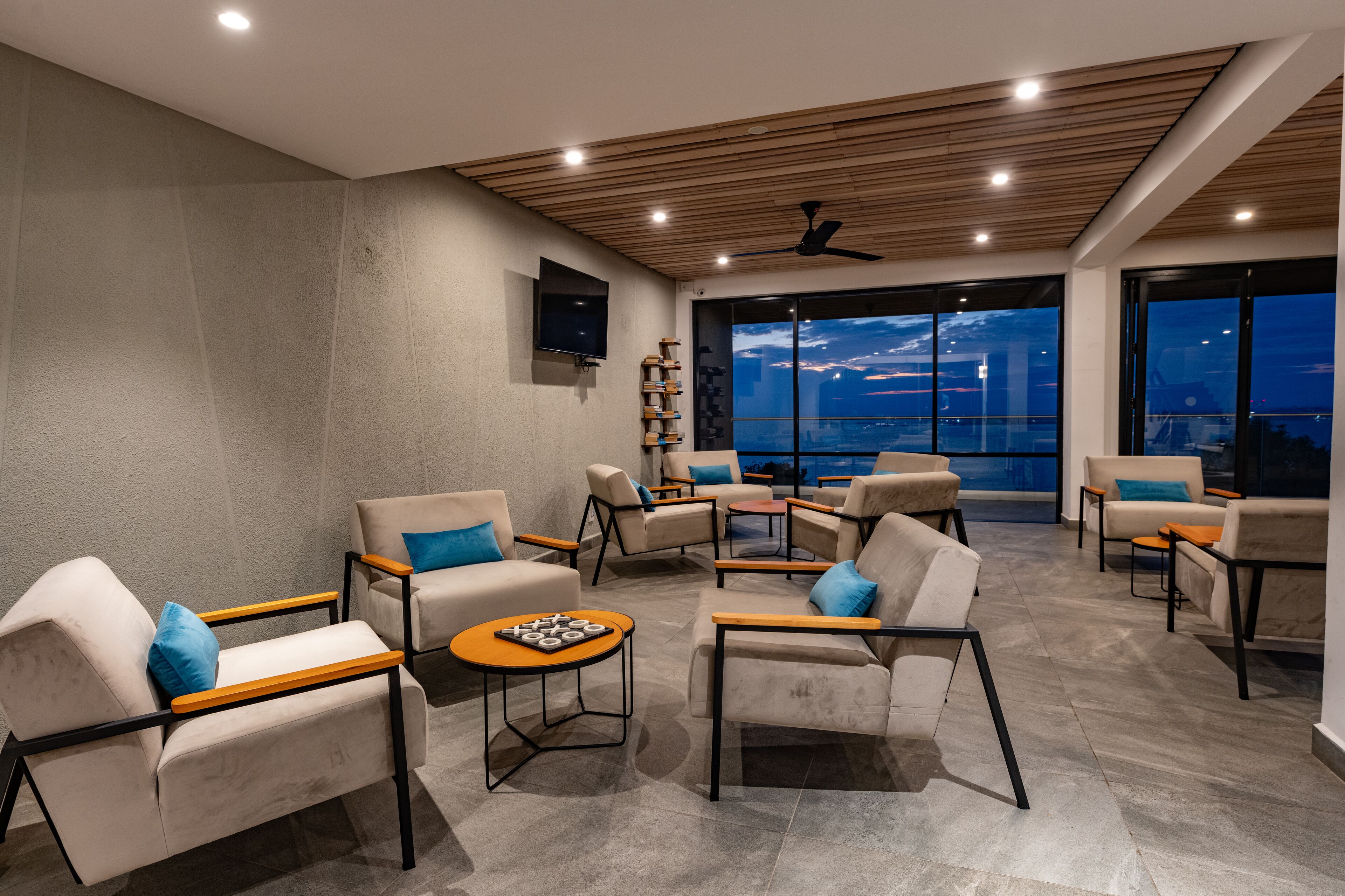 A modern lounge area with multiple seating options, a flat-screen TV, and large windows offering a city view.