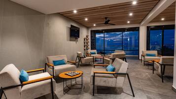 A modern lounge area with multiple seating options, a flat-screen TV, and large windows offering a city view.
