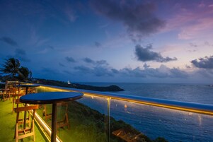 Una terrazza sul mare con tavoli e sedie, con vista sull'oceano e un'isola in lontananza.