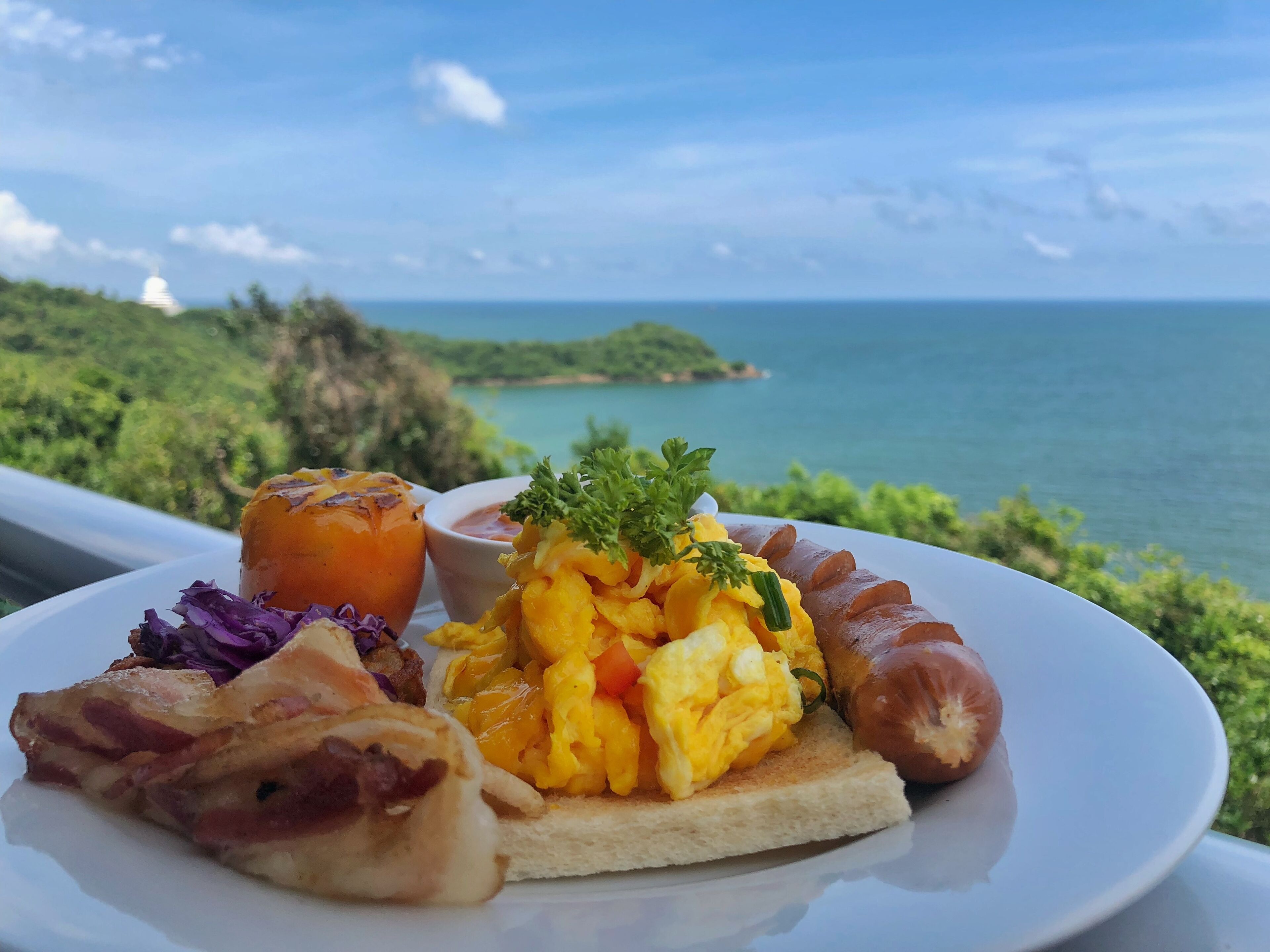 Une assiette remplie de plats pour le petit-déjeuner, avec en arrière-plan une vue imprenable sur l’océan.