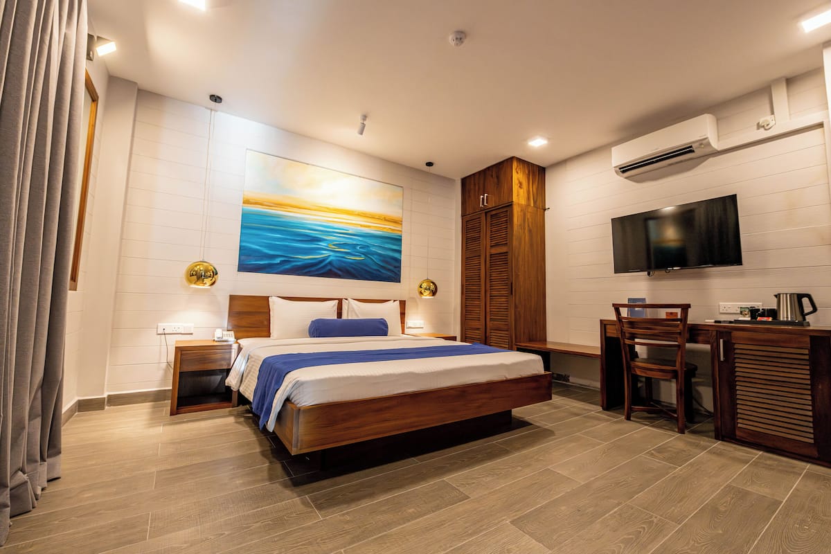A modern hotel room with a large bed, a desk with a chair, a flat-screen TV, and an air conditioning unit.