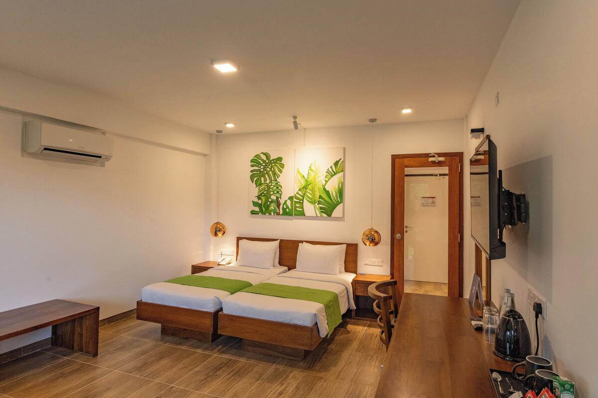 A hotel room with a double bed, bedside tables, a bench, a coffee maker, and a TV mounted on the wall.