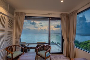 Un balcón con vista al mar, dos sillas de madera, una mesa y una puerta de vidrio.