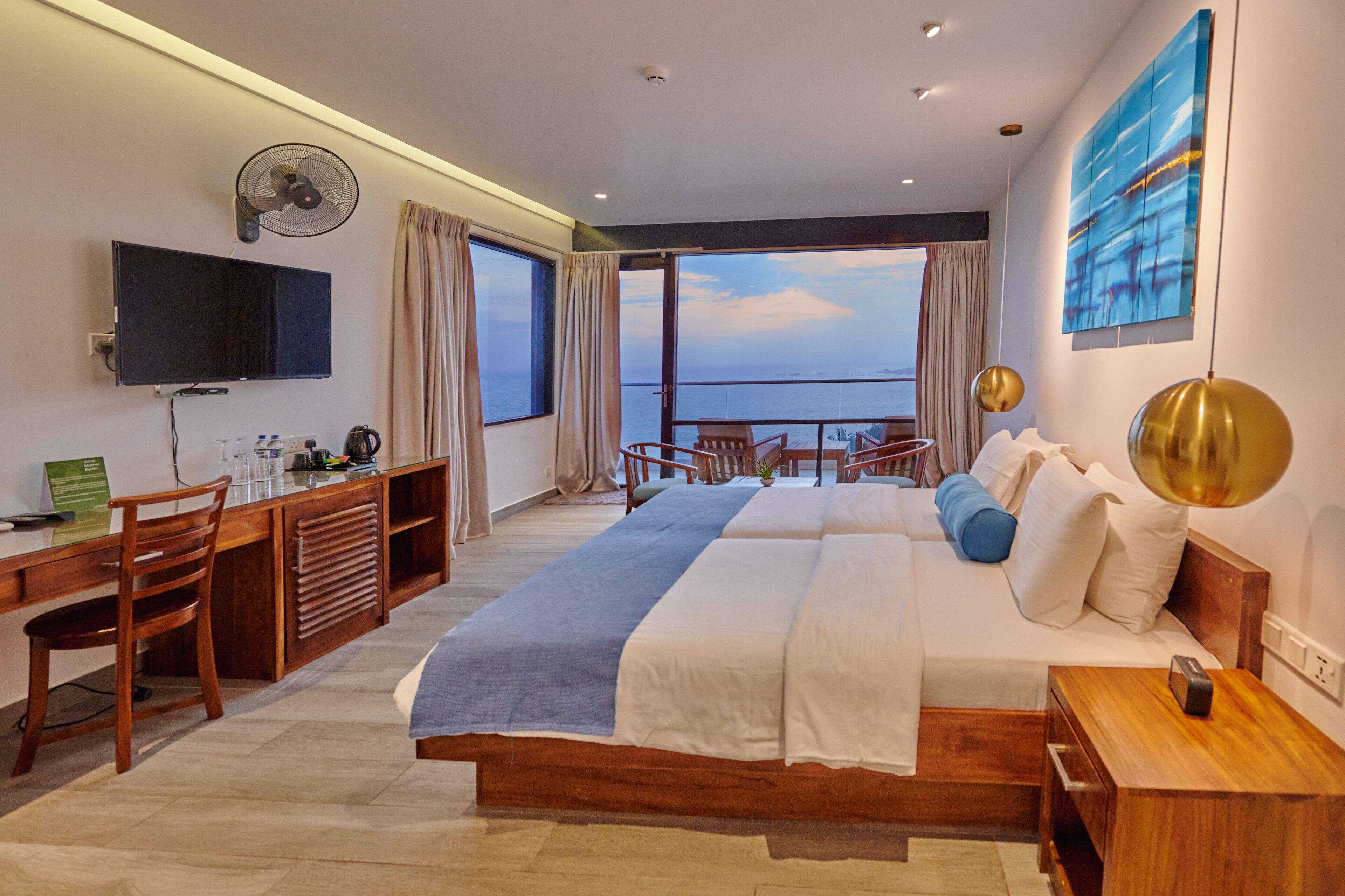 Una habitación de hotel moderna con una cama grande, un escritorio con ordenador, un televisor y un balcón con vistas al mar.