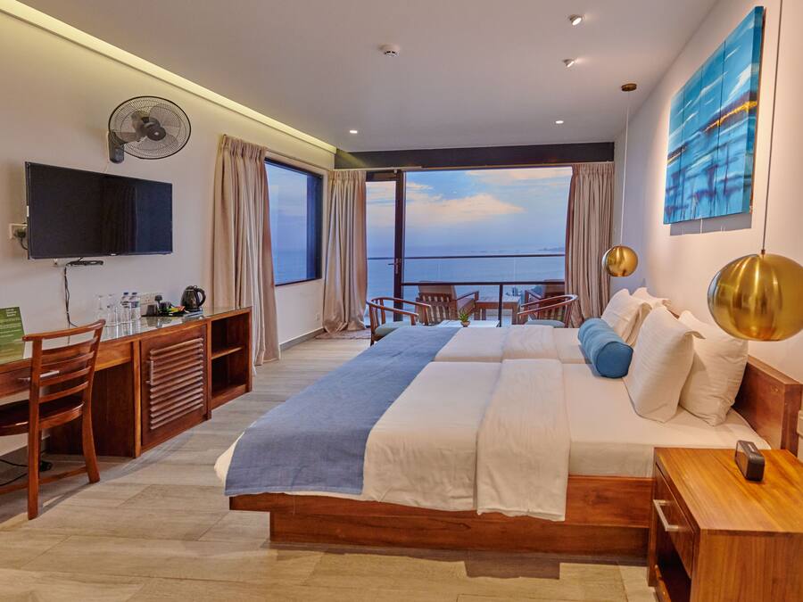 Una habitación de hotel moderna con una cama grande, un escritorio con ordenador, un televisor y un balcón con vistas al mar.