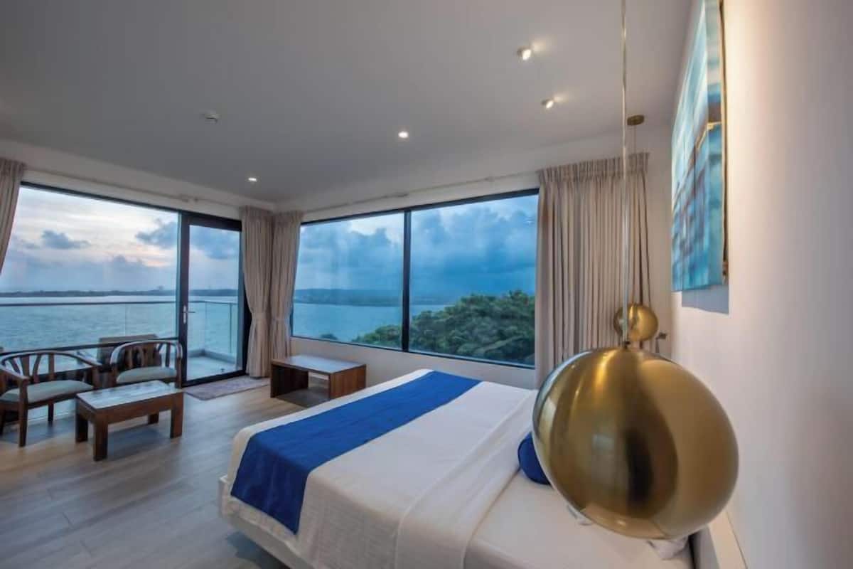 A hotel room with a large bed, a desk, and a view of the sea.