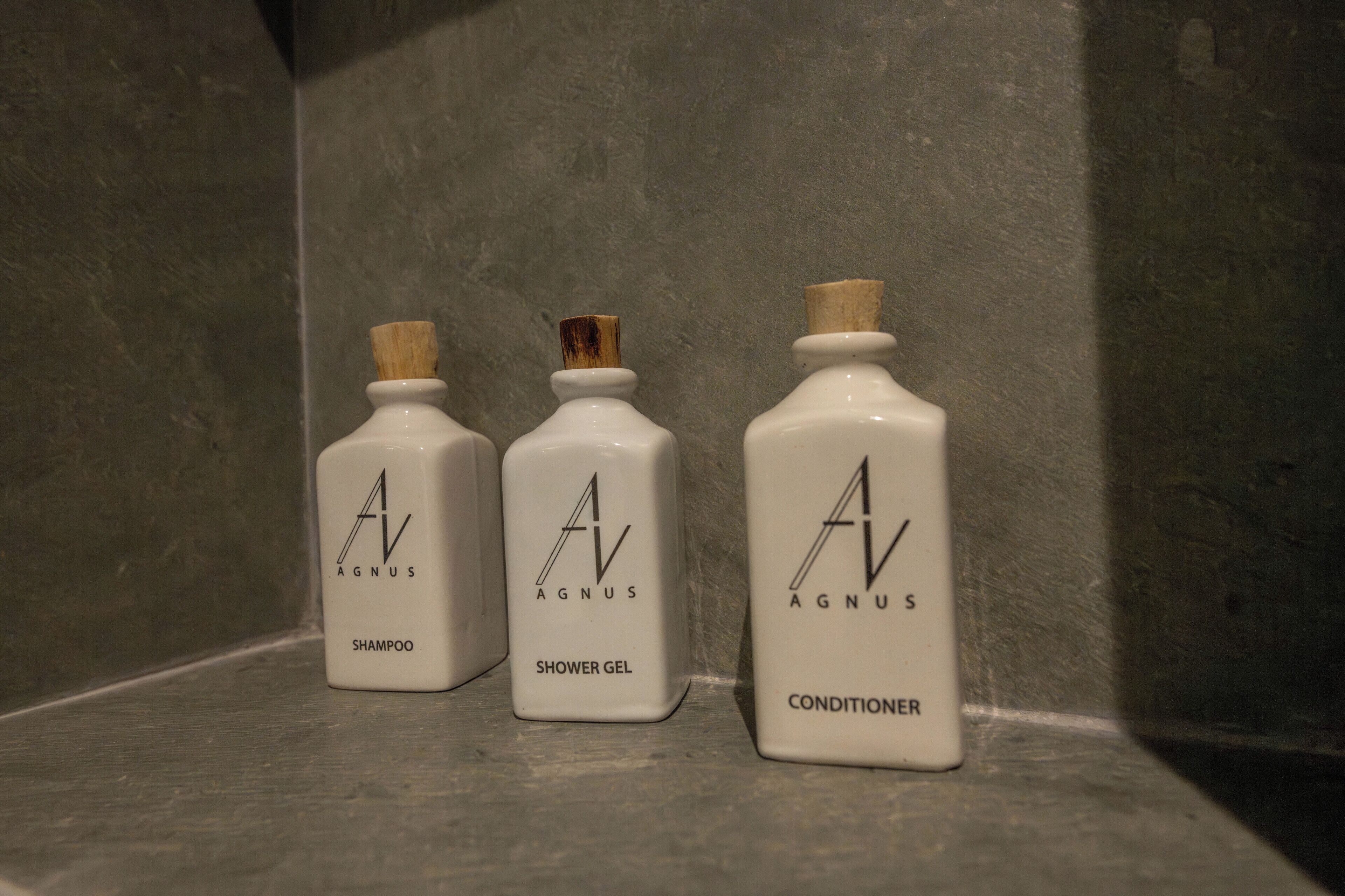 Three white bottles labeled 'AGNUS SHAMPOO', 'AGNUS SHOWER GEL', and 'AGNUS CONDITIONER' on a shelf.