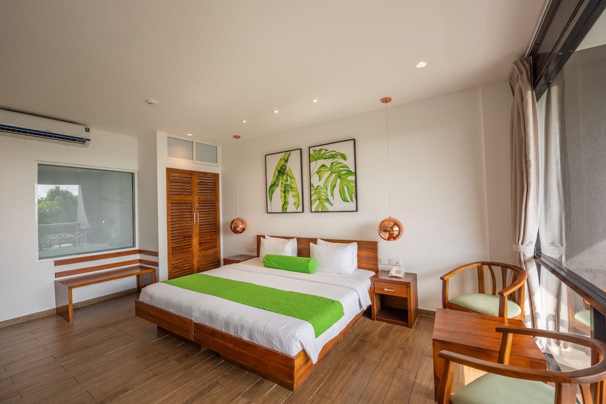 A modern hotel room with a large bed, wooden furniture, a bench, a desk, and a window with a view.